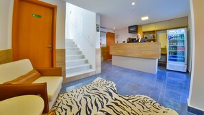 Un vestíbulo de hotel con mostrador de recepción, una escalera y una zona de estar con alfombra estampada.