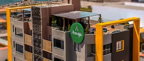 A modern multi-story building with a rooftop terrace, a sign reading "Aracaju," and a view of the ocean.