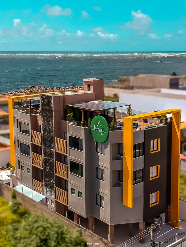 Un edificio moderno de varios pisos con terraza en la azotea, un letrero que dice "Aracaju" y vista al océano.