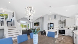 Une cuisine spacieuse dotée d’appareils électroménagers modernes, un coin repas avec des chaises bleues et un escalier menant à un espace de vie en mezzanine.