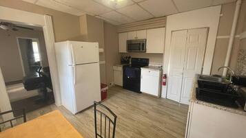 A compact kitchen with a refrigerator, microwave, and stove. There is a dining table with chairs.