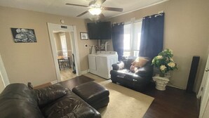 A living room with a ceiling fan, a black leather couch, a white sofa, a small table with a vase of flowers, and a kitchen area in the background. - (F1) Convenient 3br Syracuse University apartment (Syracuse)