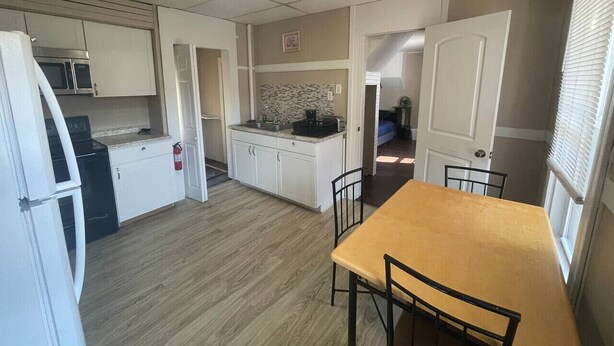 A compact kitchen with white cabinets, a microwave, and a sink. There is a dining area with a table and chairs. - (F1) Convenient 3br Syracuse University apartment (Syracuse)