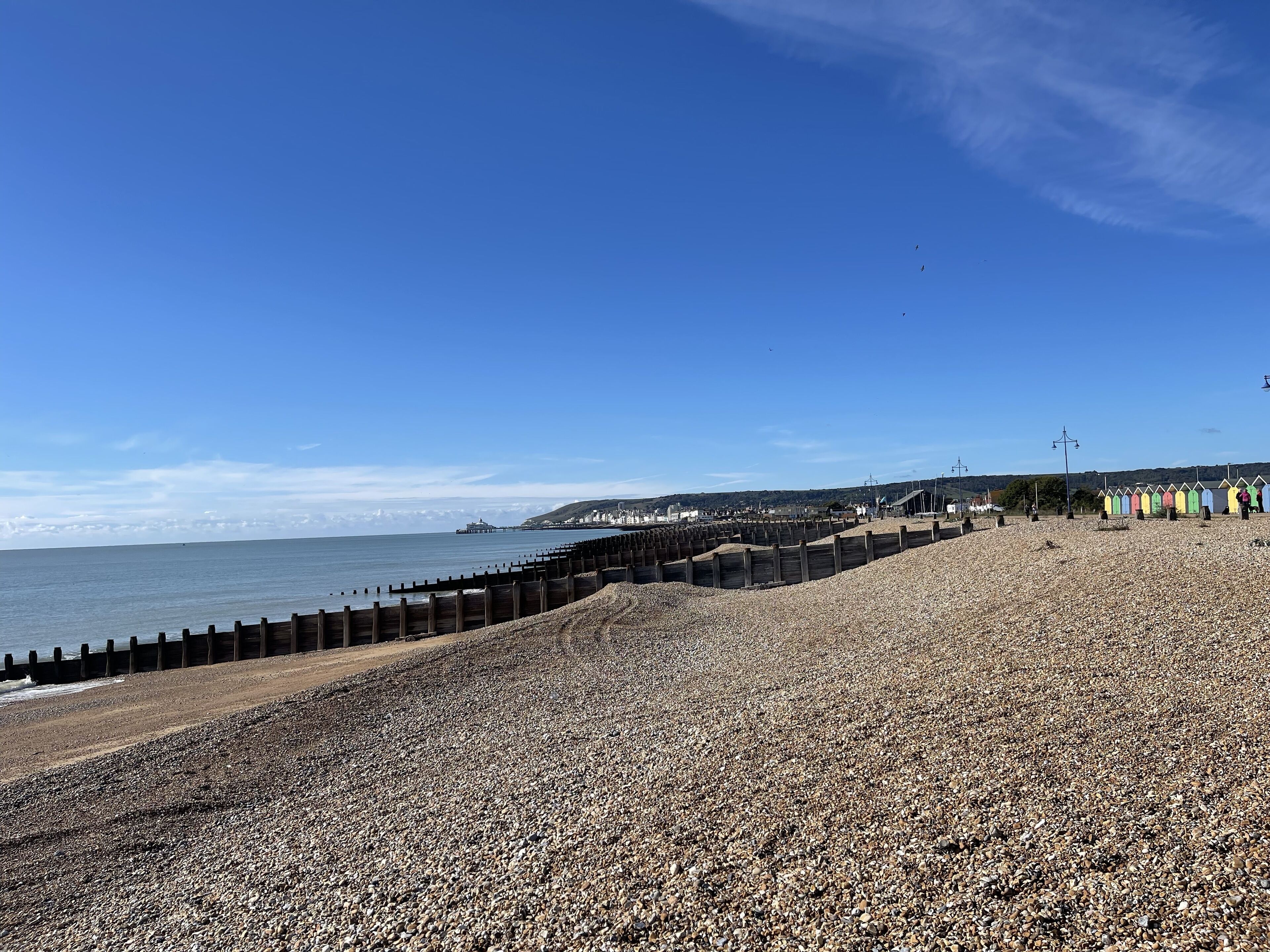 A pebbled beach with a wooden breakwater and colorful beach huts.