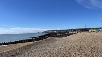 A pebbled beach with a wooden breakwater and colorful beach huts.