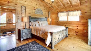 A wooden cabin bedroom with a bed, nightstands, a ceiling fan, and a window with curtains.