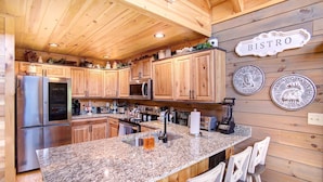 A kitchen with wooden cabinets, granite countertops, and a bar area with stools.