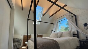 A bedroom with a bed, a window with curtains, a bedside table, and a chair. - Cozy cabin retreat nestled among forest trees (Idyllwild-Pine Cove)