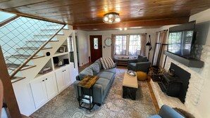 A cozy living room with a wooden ceiling, a fireplace, a sofa, a coffee table, and a staircase with a pet climbing area. - Cozy cabin retreat nestled among forest trees (Idyllwild-Pine Cove)