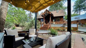 A covered outdoor seating area with wicker furniture and string lights. - Cozy cabin retreat nestled among forest trees (Idyllwild-Pine Cove)