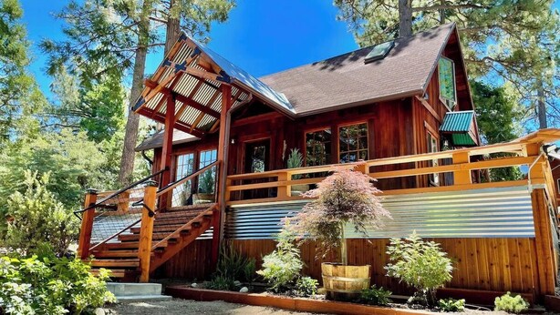 A wooden cabin with a staircase, a covered porch, and a garden with various plants. - Cozy cabin retreat nestled among forest trees (Idyllwild-Pine Cove)