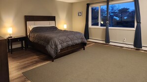 Une chambre à coucher avec un lit, deux tables de chevet, une fenêtre avec des rideaux et un tableau accroché au mur.