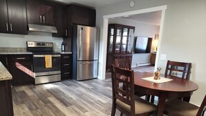 Une cuisine moderne avec des meubles de couleur bois foncé, des appareils électroménagers en acier inoxydable et un parquet en bois disposé en chevrons.