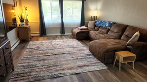 Un salon avec un canapé en cuir marron, une petite table d’appoint en bois, un tapis à motifs et une fenêtre avec des rideaux.