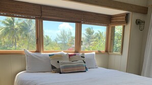 A bedroom with a large bed, wooden headboard, and a view of palm trees through the window. - Ocean view home on canal w/dock in South Bimini (Bimini)