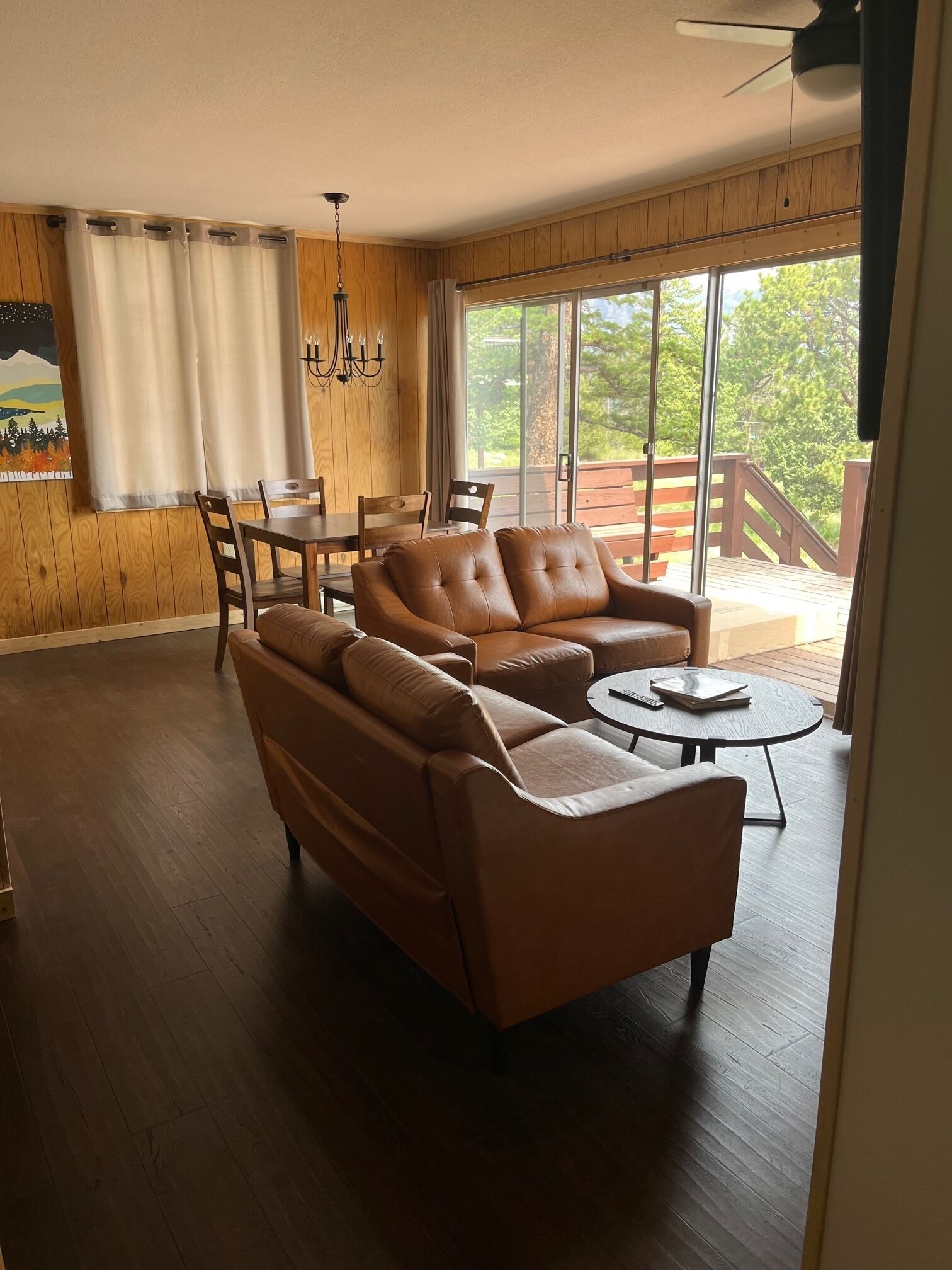 A spacious living room with a large sofa, a dining table, and chairs. There is a large window with a view of the outdoors.