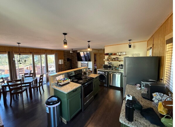Een moderne keuken met granieten aanrechtbladen, een inbouwoven en een magnetron. Er is een eethoek met een tafel en stoelen, en een prullenbak is zichtbaar.