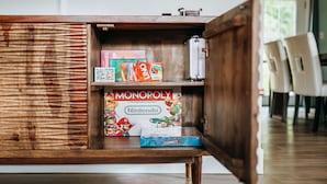 A wooden cabinet with a Nintendo Monopoly game box and other board games. - Eye-catching Home and Yard w/ Luxurious Hot Tub, Patio, and Private Trail Access (Port Angeles)