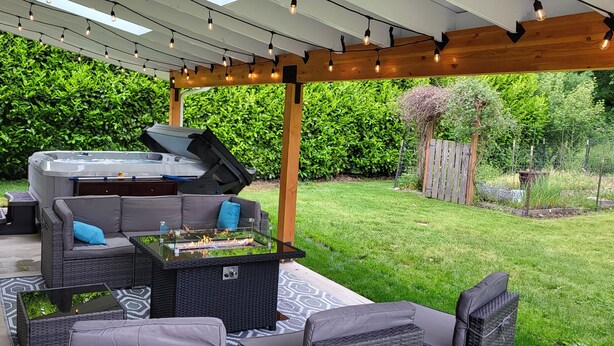 An outdoor patio with a barbecue grill, seating area, and a pergola with string lights. - Eye-catching Home and Yard w/ Luxurious Hot Tub, Patio, and Private Trail Access (Port Angeles)