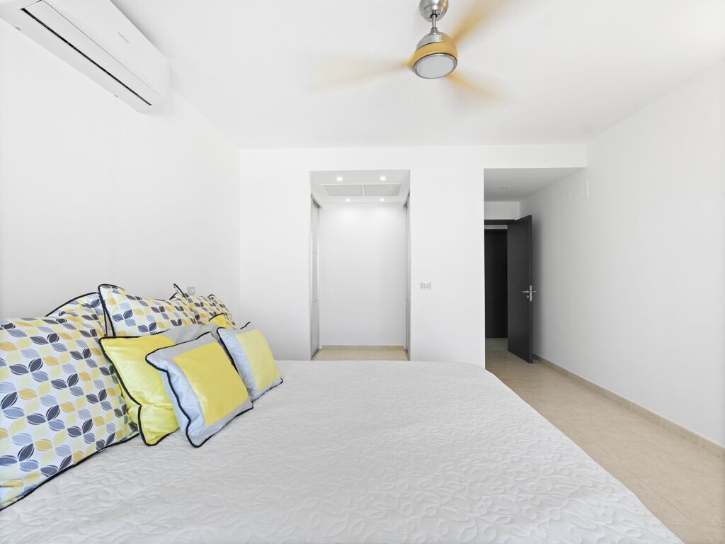 A bedroom with a bed, pillows, an air conditioner, a ceiling fan, and a hallway leading to a door.