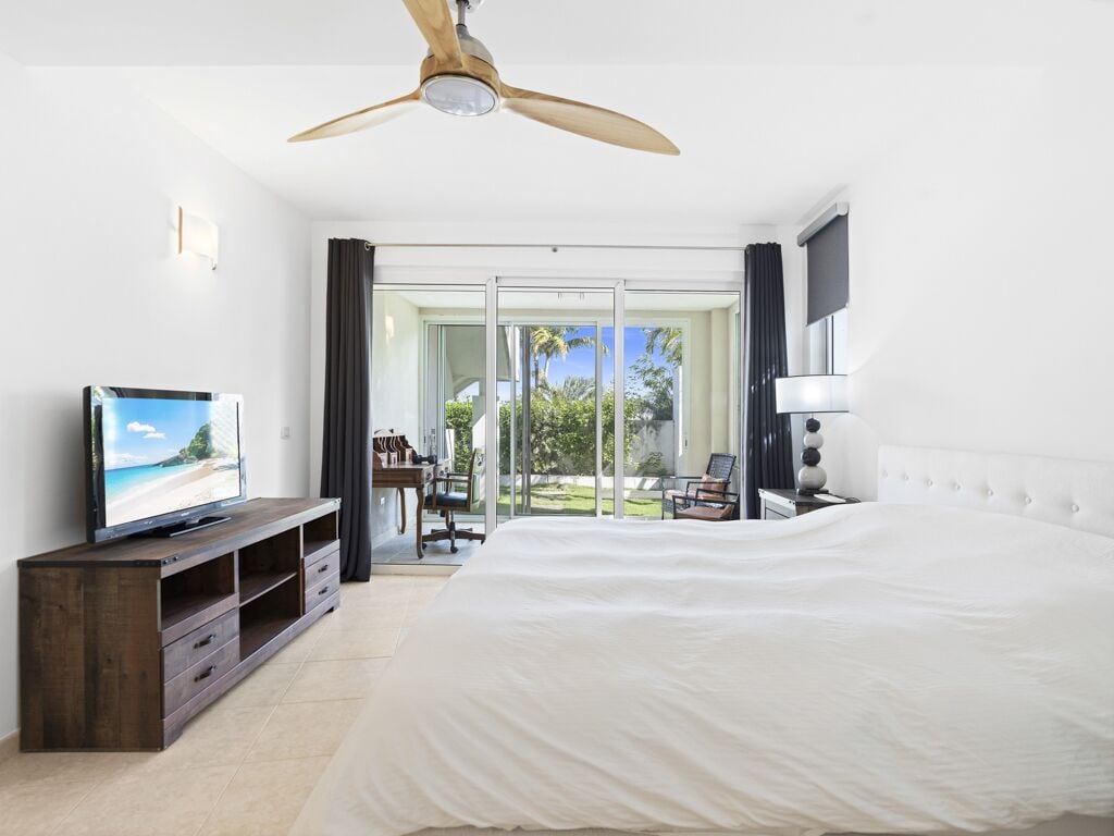 Une chambre avec un grand lit, un téléviseur posé sur un meuble en bois, un ventilateur de plafond et une vue sur l’extérieur grâce à une porte vitrée.