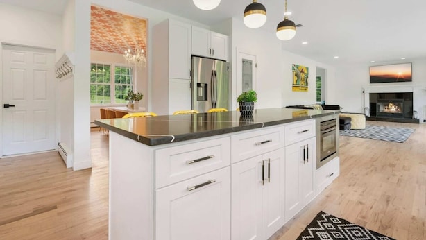 A modern kitchen with white cabinets, a central island, stainless steel appliances, pendant lighting, and a fireplace.