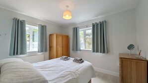 Een slaapkamer met een bed, een kledingkast, een raam met gordijnen en een nachtkastje met een lamp.