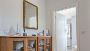 Een gang met een houten kast, een spiegel en een deur naar een andere kamer.