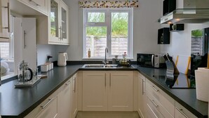 Een moderne keuken met witte kastjes, een zwart aanrecht, een dubbele spoelbak, een koffiezetapparaat, een magnetron en een raam met uitzicht op groen.