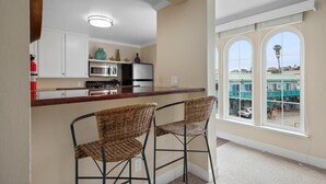 A kitchen with a bar area, two wicker chairs, and a view of a building through large windows.