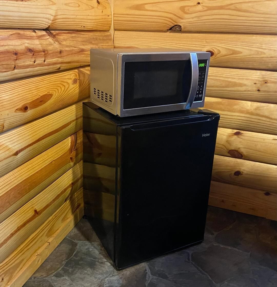 Un refrigerador compacto negro con un microondas encima, ubicado frente a una pared de madera y un piso de piedra.