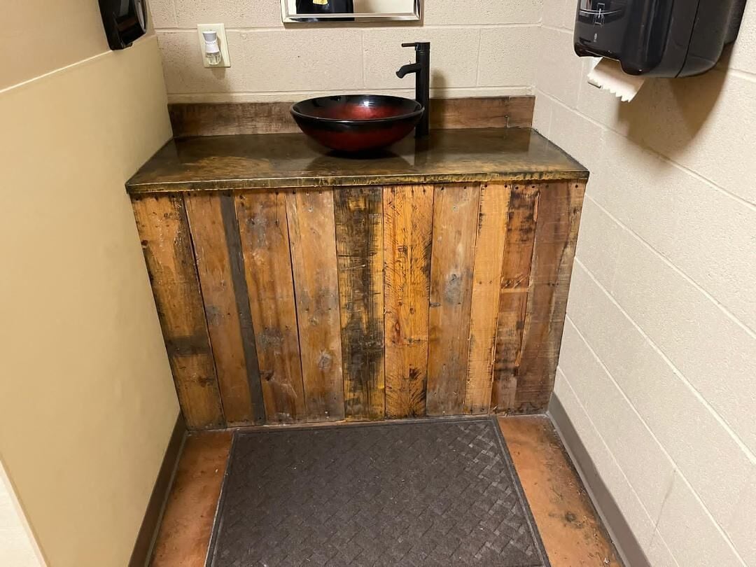 A small bathroom with a wooden vanity, a black sink, and a black mat on the floor.