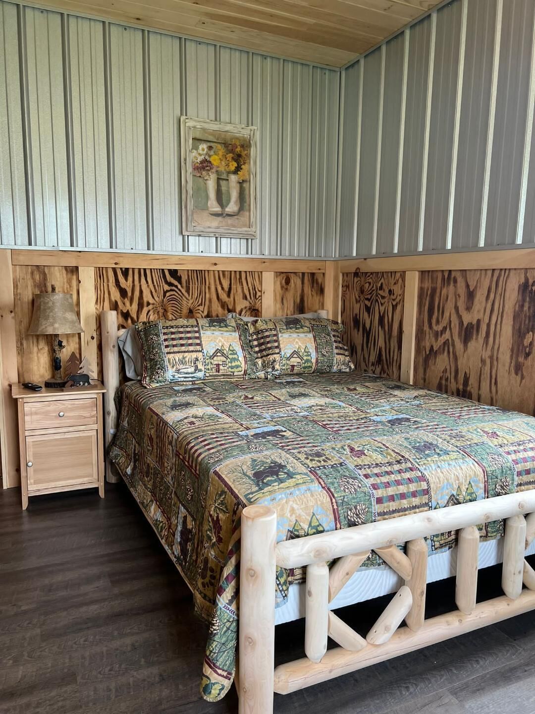 Un dormitorio con estructura de cama de madera, una mesita de noche con lámpara y un cuadro en la pared.