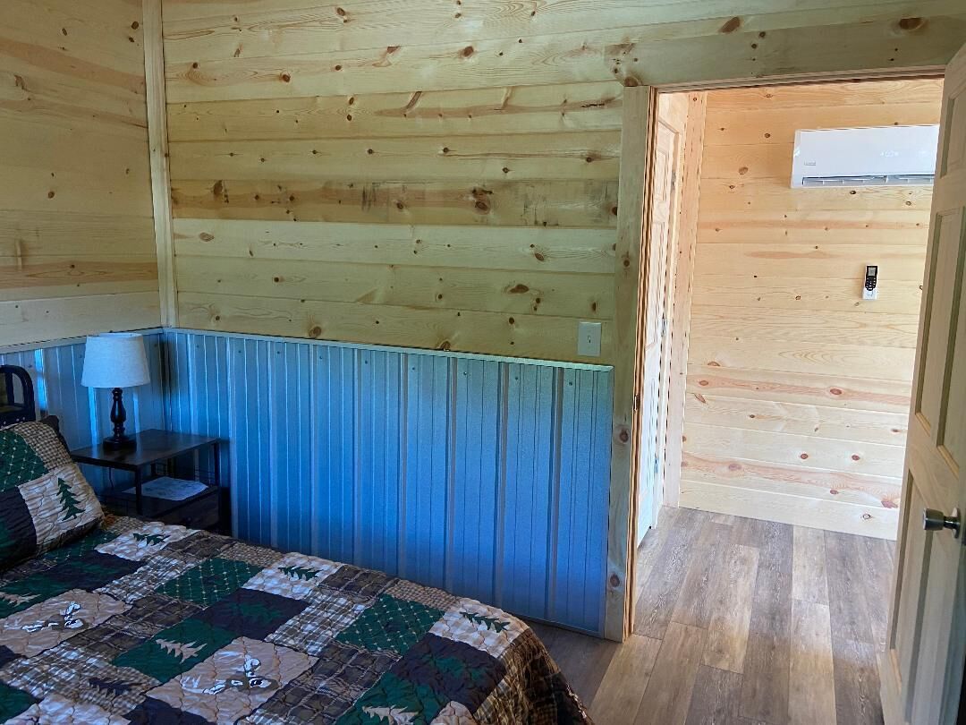 A wooden cabin room with a bed, a nightstand, a lamp, and a door.