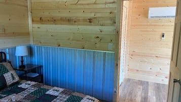 A wooden cabin room with a bed, a nightstand, a lamp, and a door.