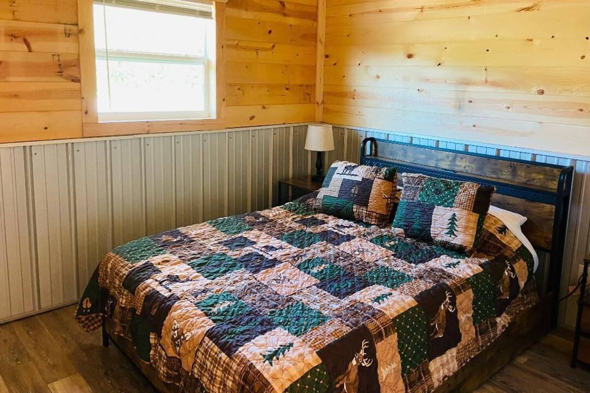 Une chambre dans une cabane en bois, avec un lit, une fenêtre et une lampe.