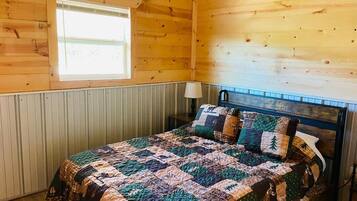 Een slaapkamer in een houten blokhut met een bed, een raam en een lamp.
