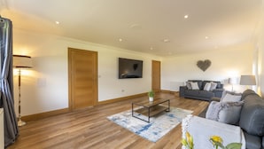Una sala de estar moderna con piso de madera, un sofá gris, una mesa de centro y un televisor montado en la pared.