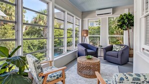 A sunlit room with large windows, a blue sofa, a wicker ottoman, and a patterned armchair. - Cozy Family Home Close to the Beach (Tybee Island)