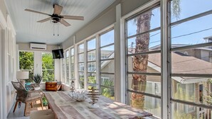 A sunlit room with a wooden table, wicker chairs, and a large window overlooking a residential area. - Cozy Family Home Close to the Beach (Tybee Island)