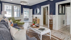 A modern living room with a blue accent wall, a white sofa, a green armchair, and a coffee table with a book. - Cozy Family Home Close to the Beach (Tybee Island)