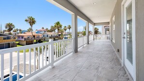 A covered balcony with a view of neighboring houses and palm trees. - Luxury Coastal Escape • Heated Pool & Hot Tub • 2 Min Walk to Beach (South Padre Island)