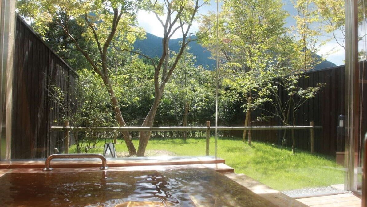 A hot tub with a view of a grassy area and trees, a wooden fence, and a mountain in the background.