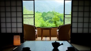 Una habitación japonesa tradicional con suelo de tatami, una mesa baja con tetera y tazas, y vistas a un paisaje verde exuberante a través de amplias ventanas.