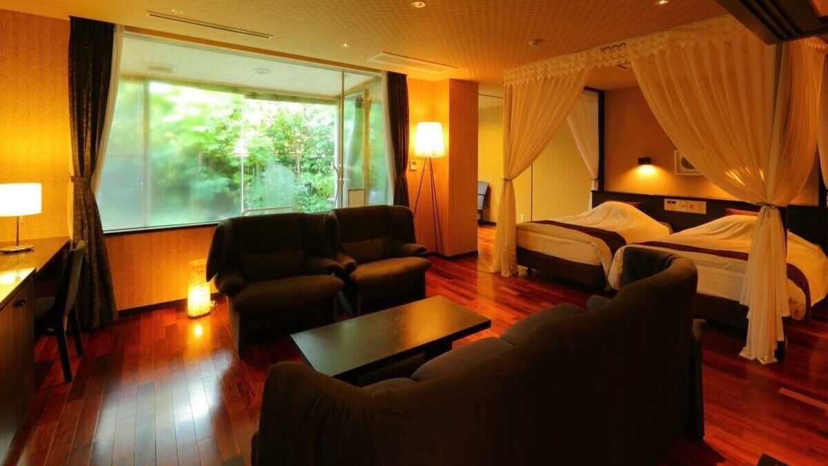 Habitación de hotel con un ventanal grande, cama con dosel, sofá y una mesita.