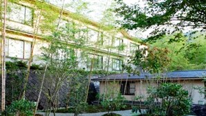 Un edificio de estilo japonés tradicional con un jardín que presenta senderos de grava, bambú y árboles pequeños.