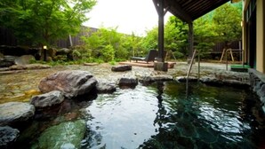 Un área de piscina al aire libre tranquila con rocas y una pérgola de madera.