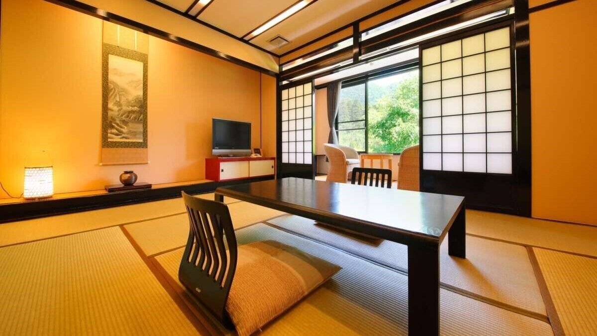 A traditional Japanese room with tatami flooring, a low table, a television, and sliding doors.