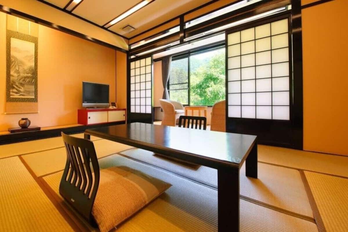 A traditional Japanese room with tatami flooring, a low table, a television, and sliding doors.