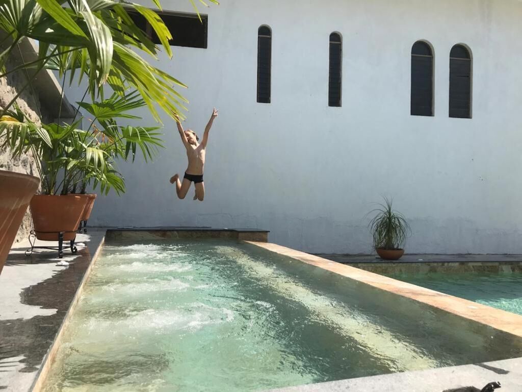 A person jumping into a pool with a white building and arched windows in the background.
